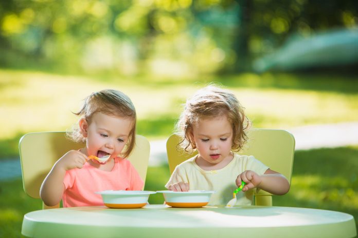 deux-petites-filles-assises-table-manger-ensemble-contre-pelouse-verte